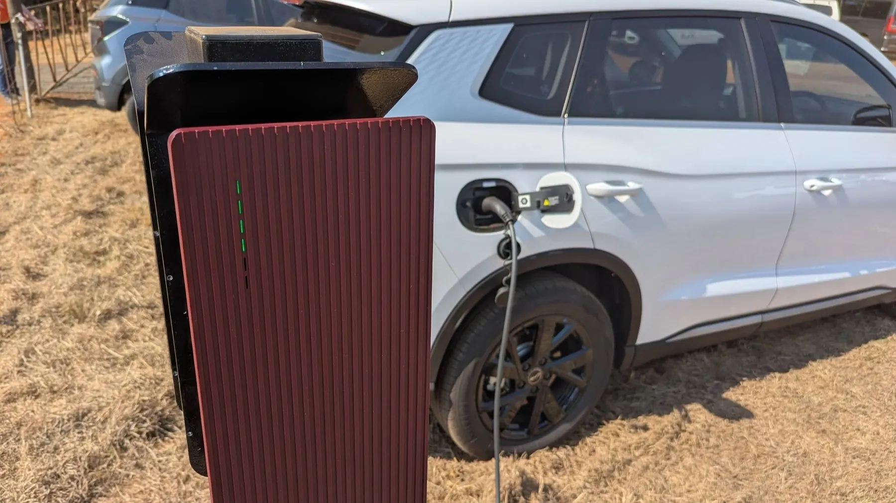 Close-up of a charge post with its status light lit green while a white SUV charges beside it