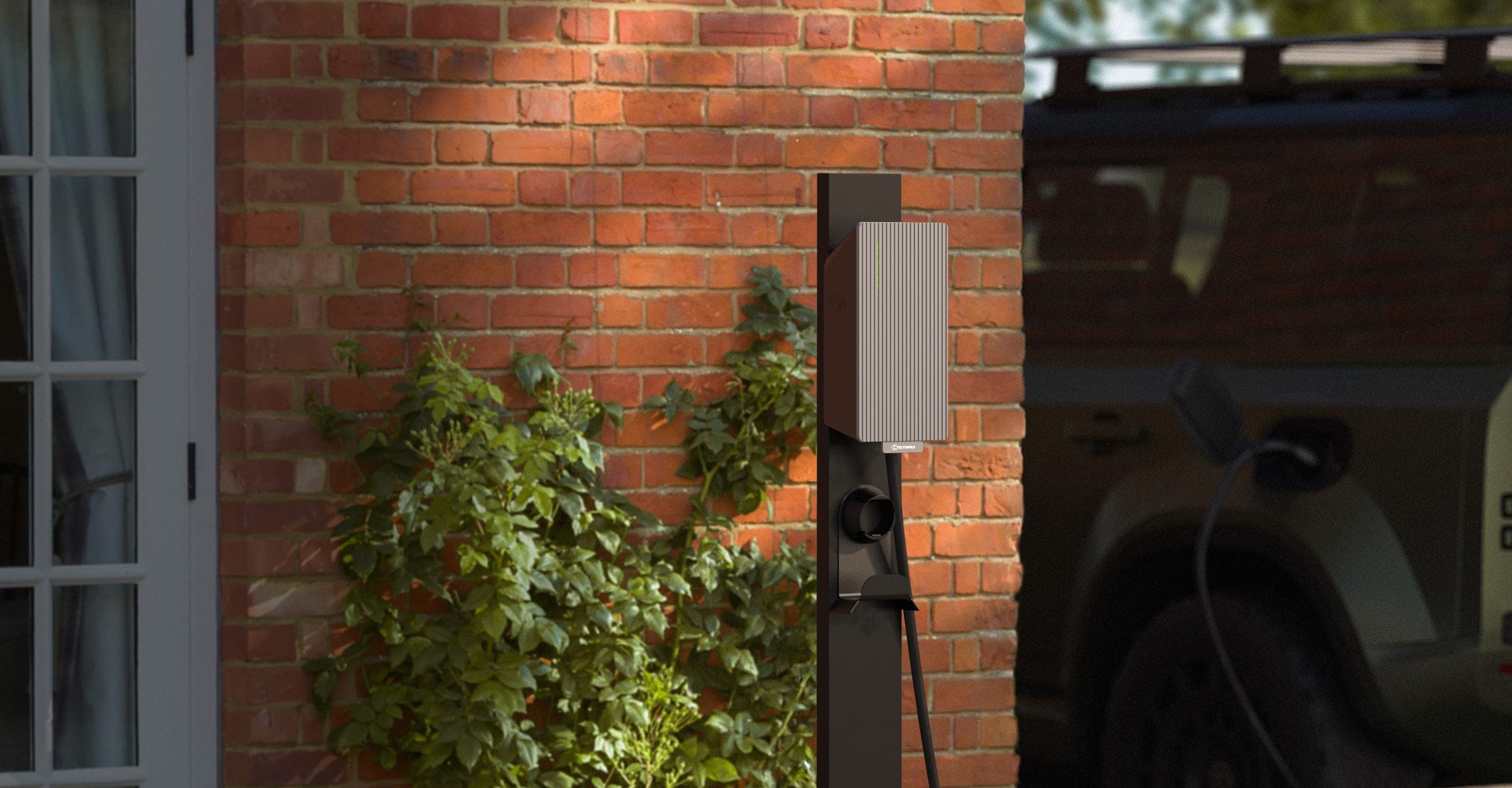 A TeltoCharge AC EV charger on a brick wall next to a parked car